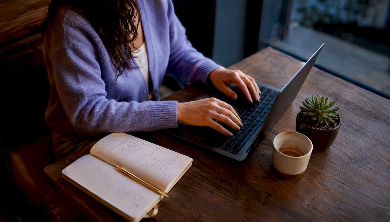 Vue de dessus de mains en train de saisir des données comptables sur ordinateur, entourées de documents et de calculatrices.