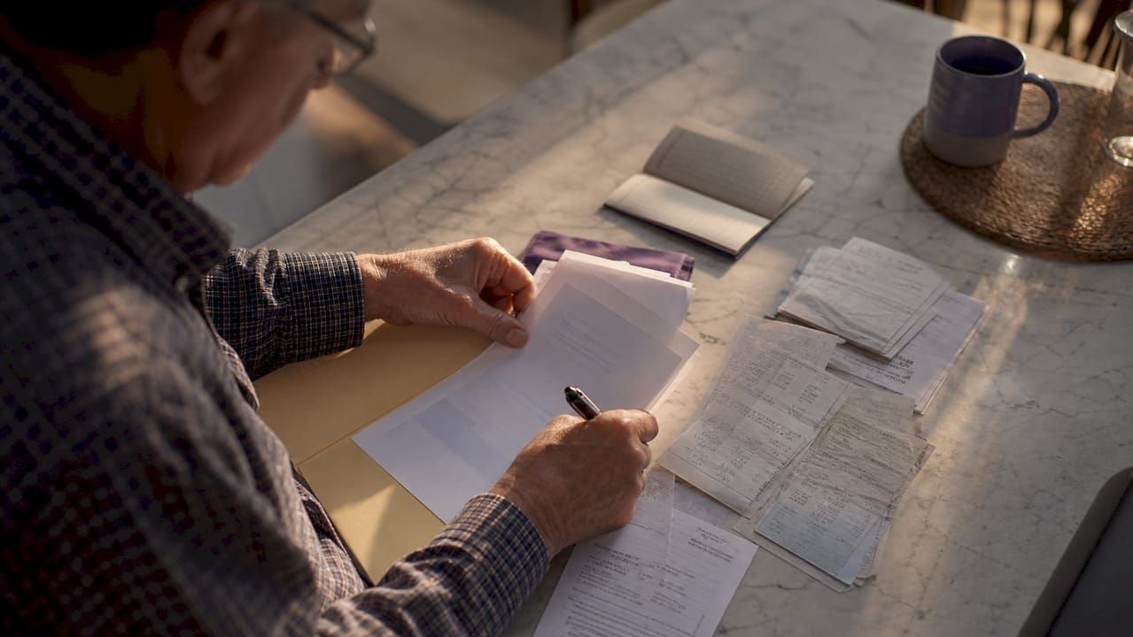 Des mains qui passent en revue des factures et des relevés de compte, cherchant à faire le tri dans les papiers administratifs.